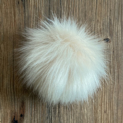 Cream fluffy pom-pom on a wooden surface