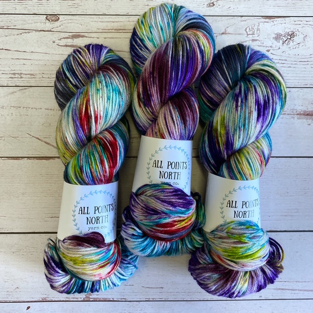 Three skeins of multicoloured yarn with All Points North labels on a white wood background