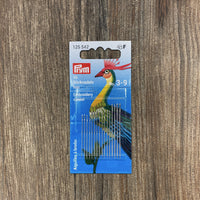 Pack of embroidery needles with a colorful bird design on the packaging against a wooden background