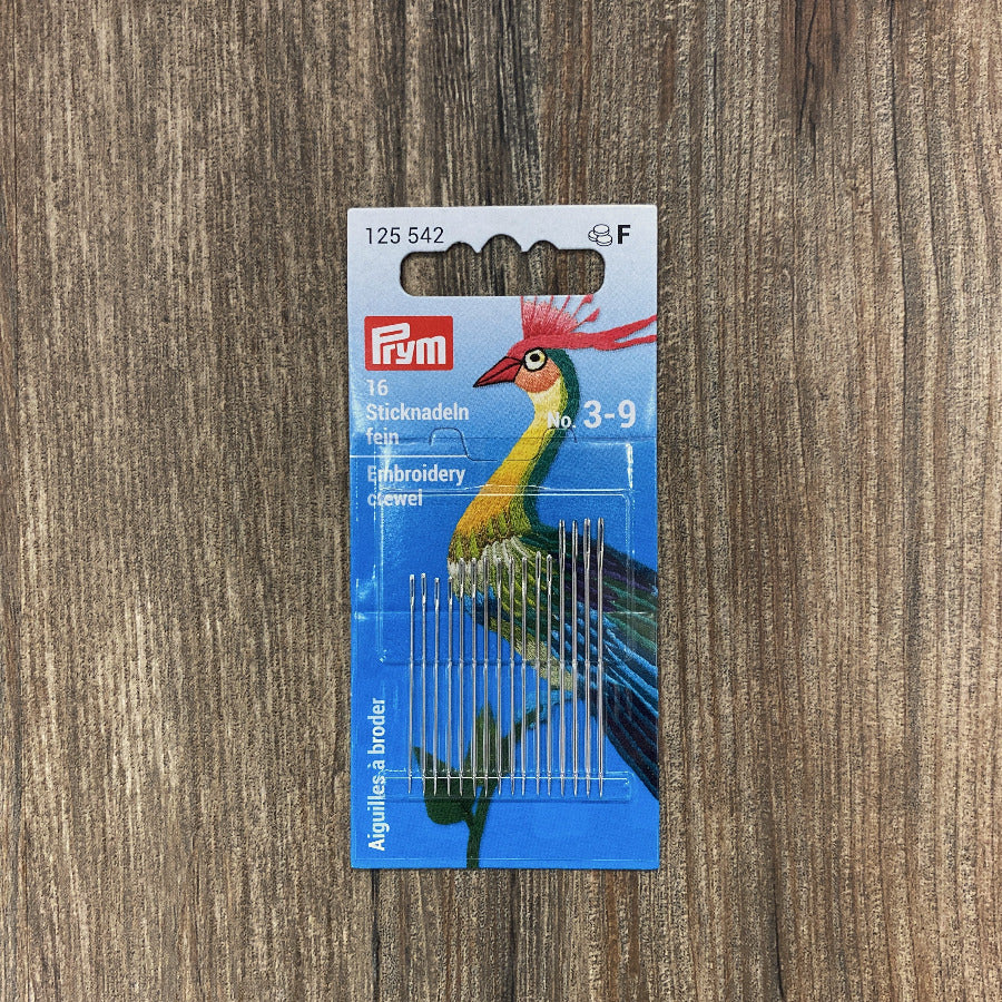 Pack of embroidery needles with a colorful bird design on the packaging against a wooden background