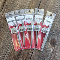 Five packaged QUADS stainless knitting needles arranged in a fan shape on a rustic wooden surface. 