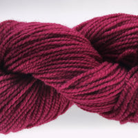 Close-up of a skein of dark burgundy pink yarn on a white background