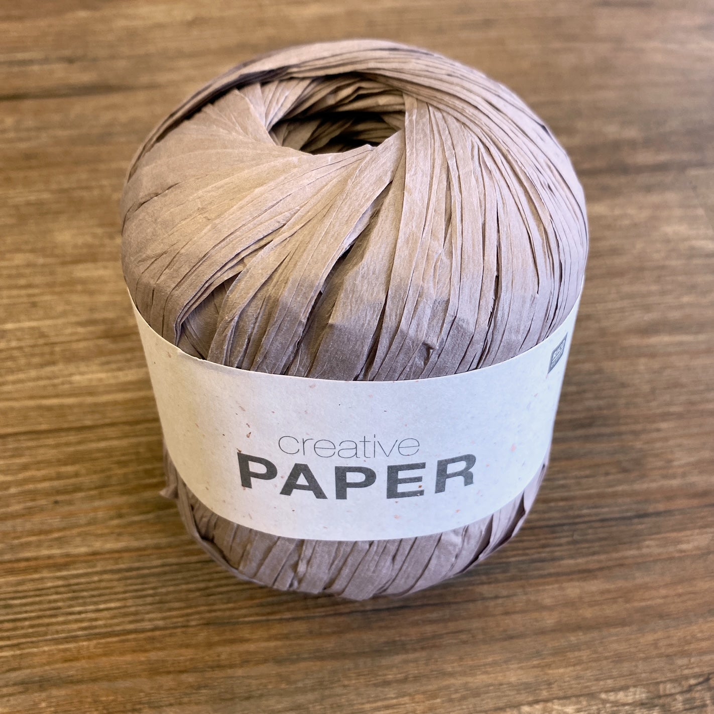 A ball of beige paper yarn with a Creative Paper label on a wood background