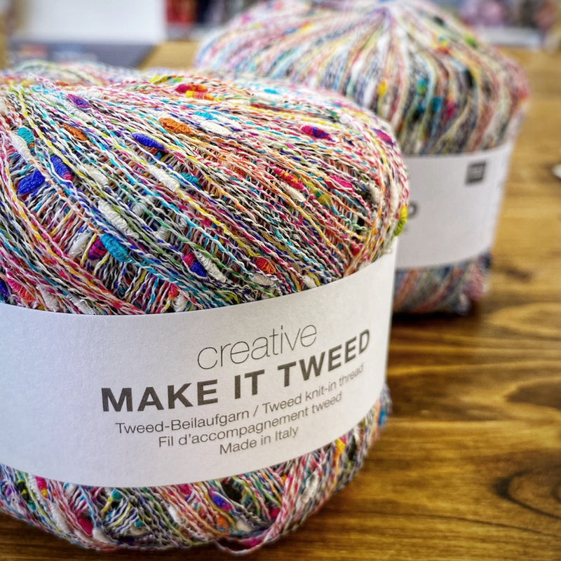 Balls of ulticoloured yarn with Creative Make It Tweed labels on a wood surface