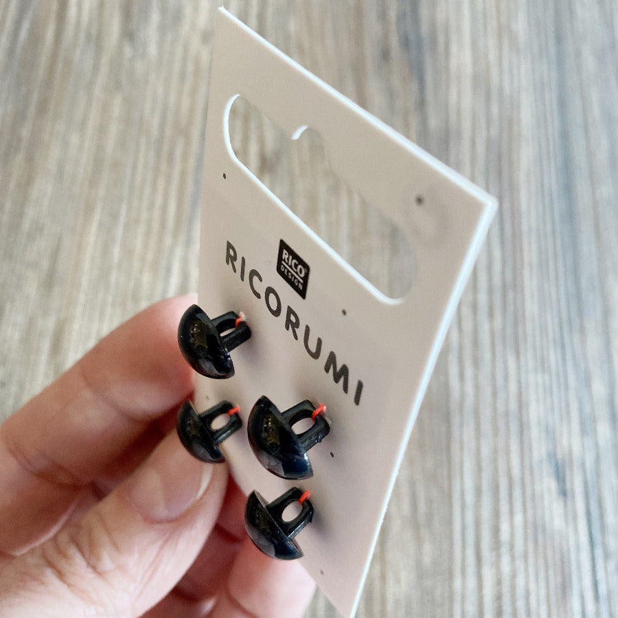 A side view of 4 black plastic button eyes on a white card, being held in a hand
