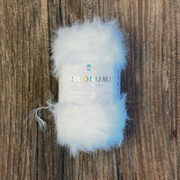 Close up of a tiny white, furry ball of yarns with a white label on a wood background