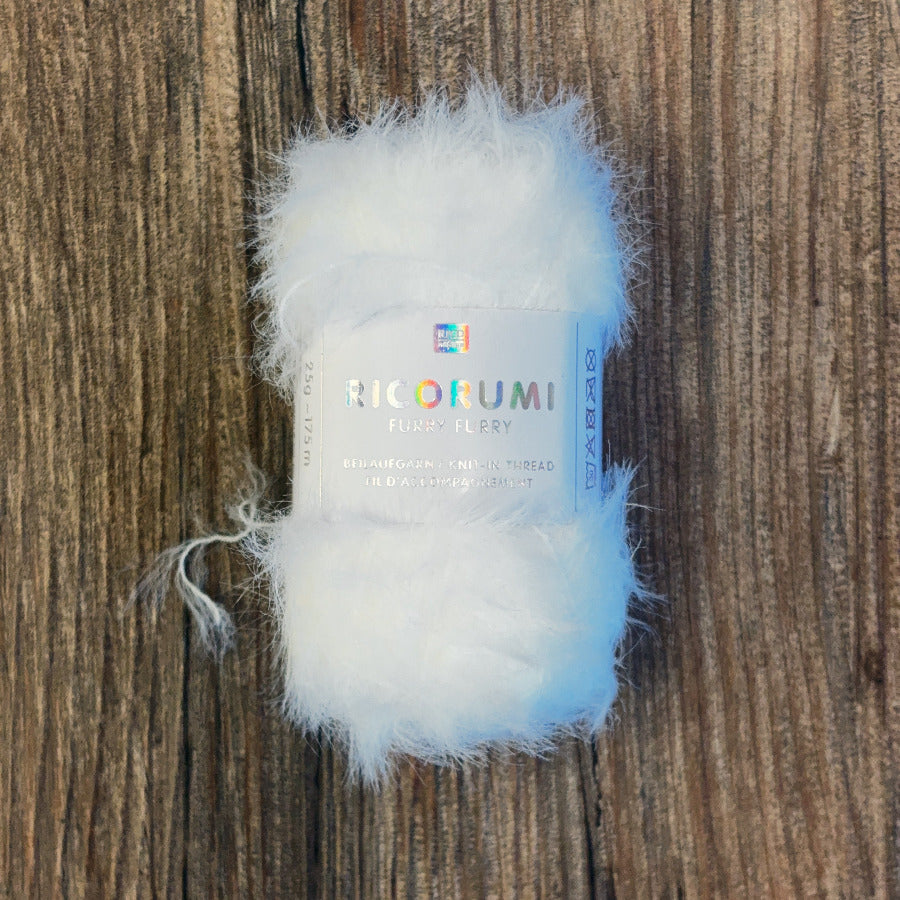 Close up of a tiny white, furry ball of yarns with a white label on a wood background
