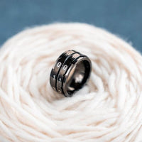 Black metal finger ring with numbers on it, displayed on a white ball of yarn with a blue background
