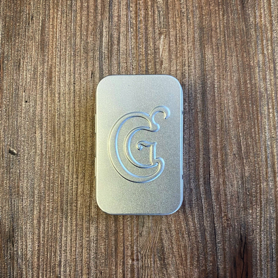 Metallic rectangular tin with a letter 'G' on a wooden surface