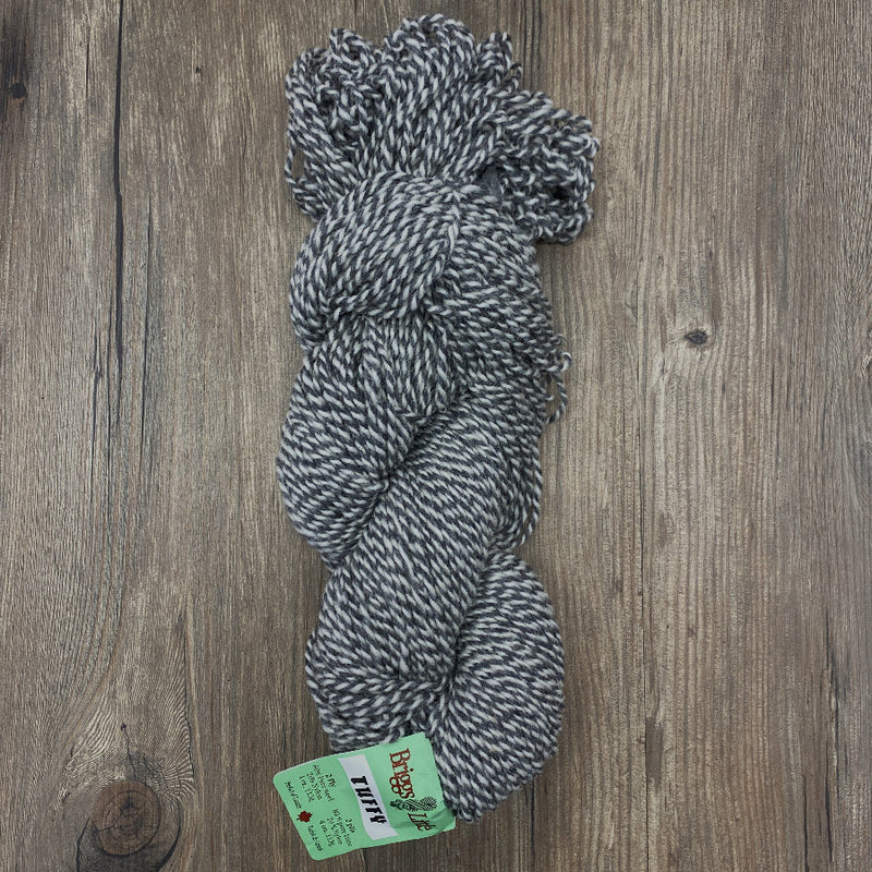 Twisted skein of grey and white yarn with a green label on a wooden surface