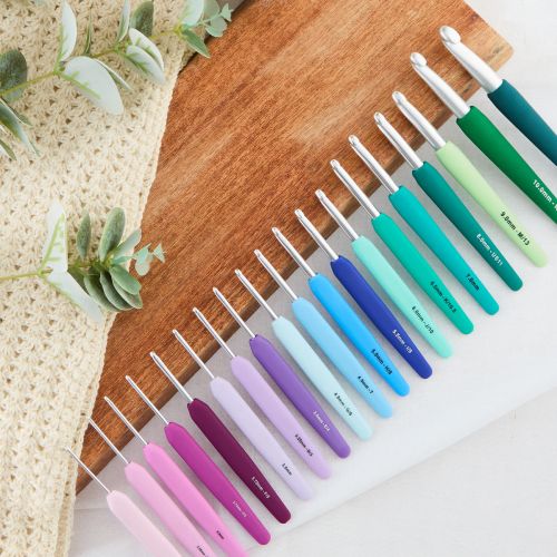 Set of colorful crochet hooks on a wooden board with a crochet swatch and leaves in the background.