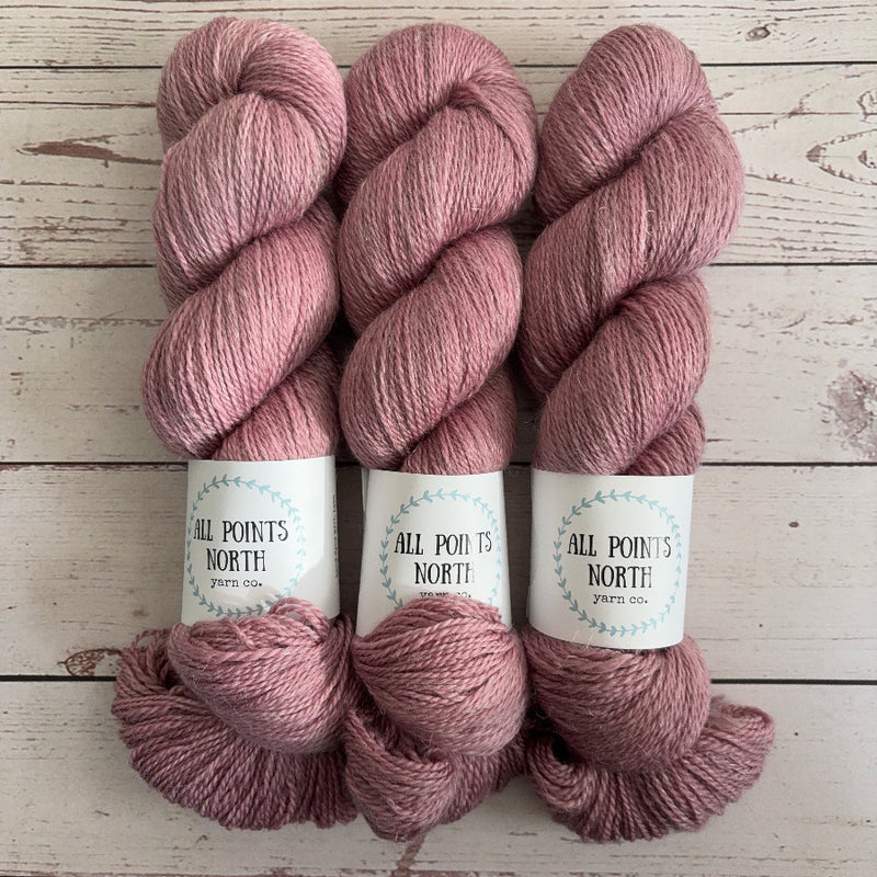 Three skeins of antique pink yarn with white labels on a white wood background