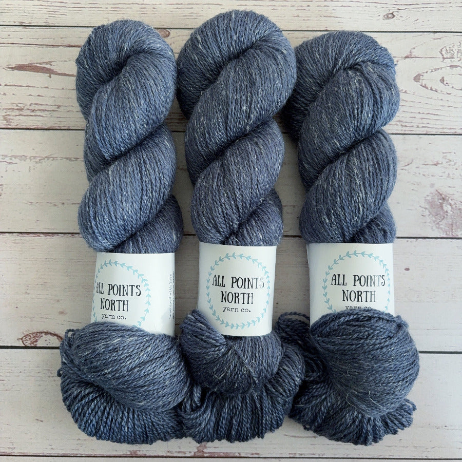 Three skeins of heathered navy yarn with white labels on a white wood background