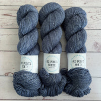 Three skeins of heathered navy yarn with white labels on a white wood background