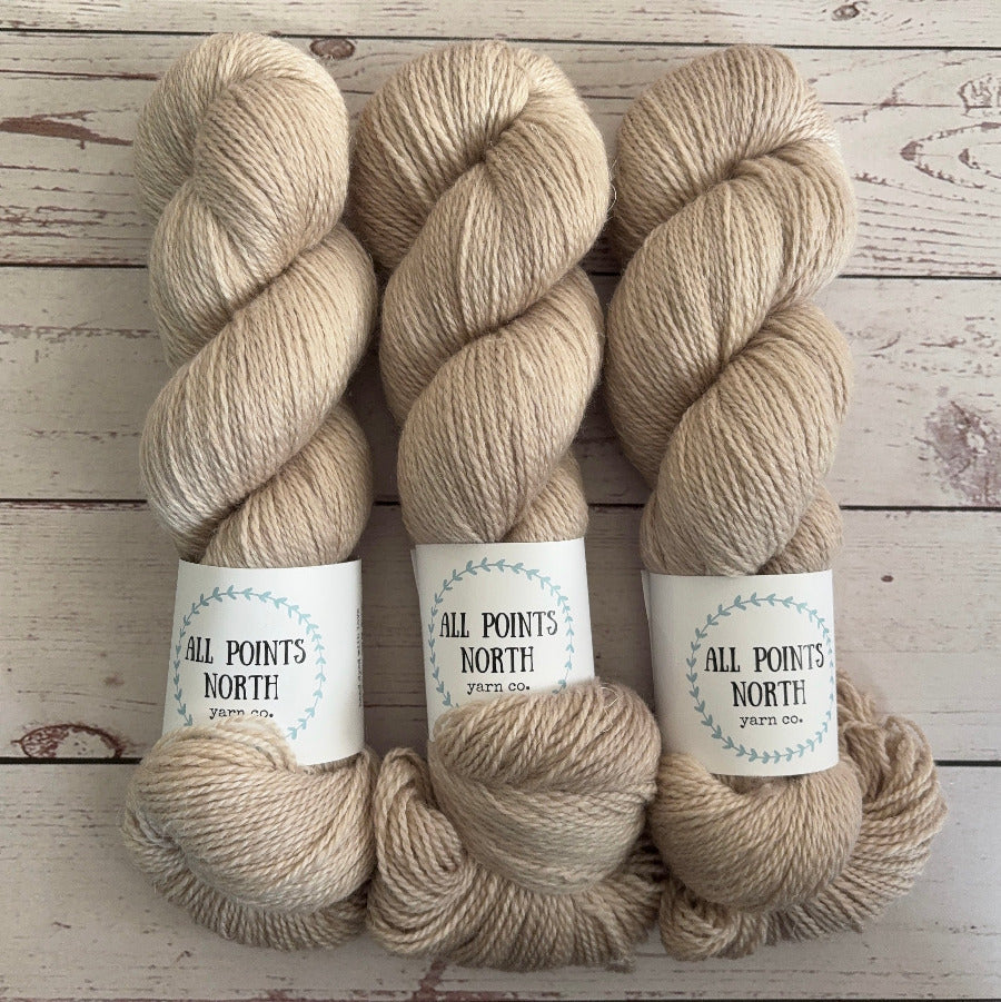 Three skeins of beige yarn with white labels on a white wood background
