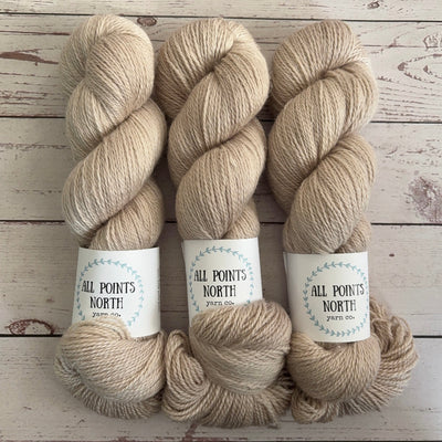 Three skeins of beige yarn with white labels on a white wood background