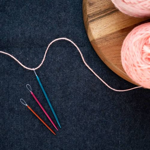 Pink yarn with wool needles on a dark surface